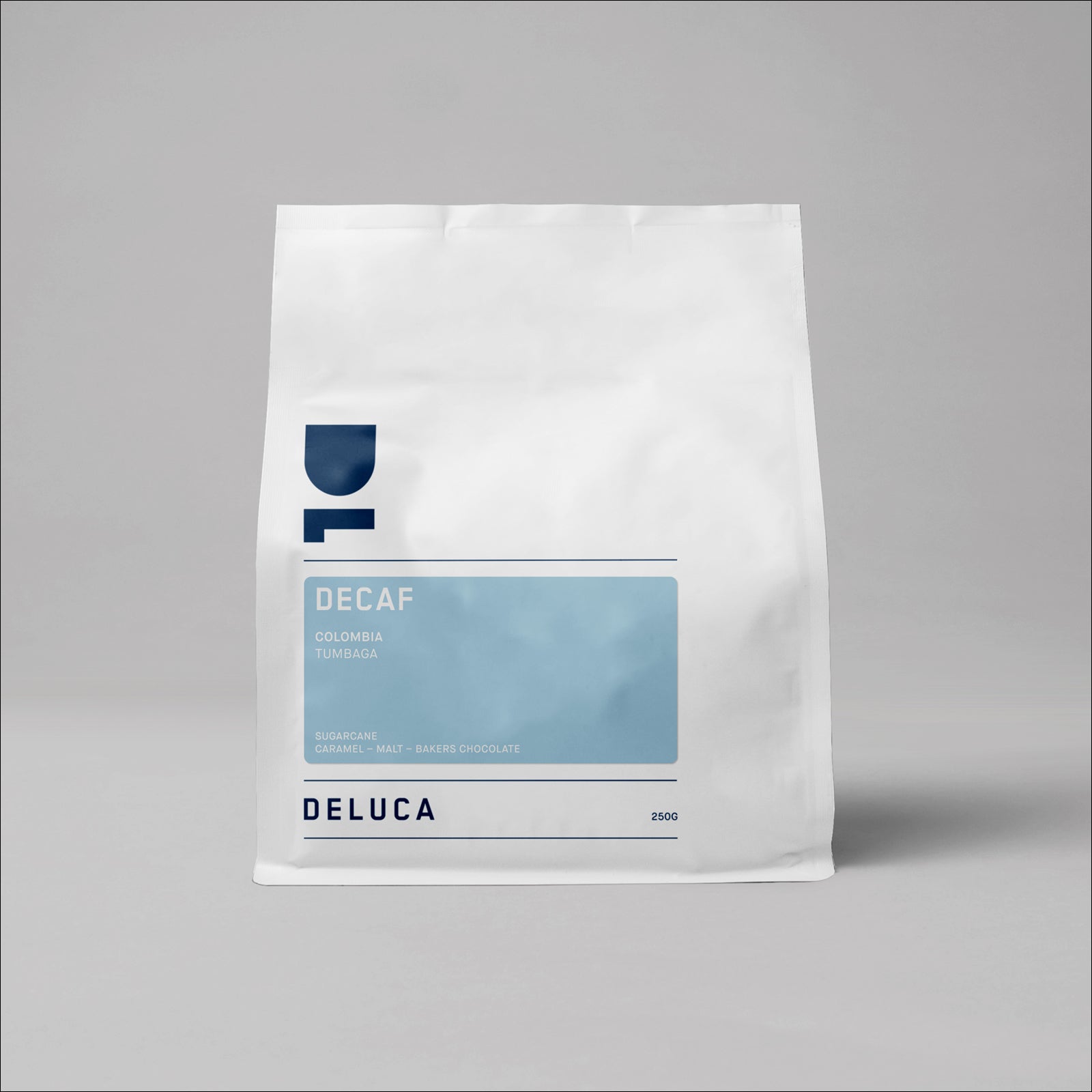 Bag of Deluca Colombia Tumbaga Decaf coffee beans in a white stand-up pouch on a grey background.