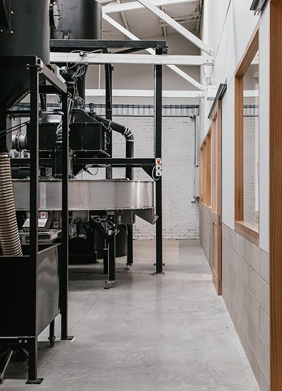 Industrial coffee roastery interior with coffee roasting equipment and concrete floor.