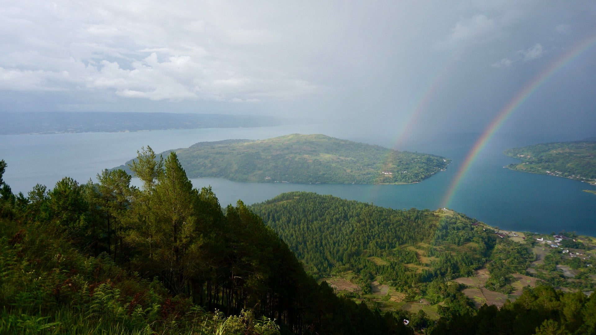 Lush green landscape with a lake and rainbow, viewed from a high vantage point.